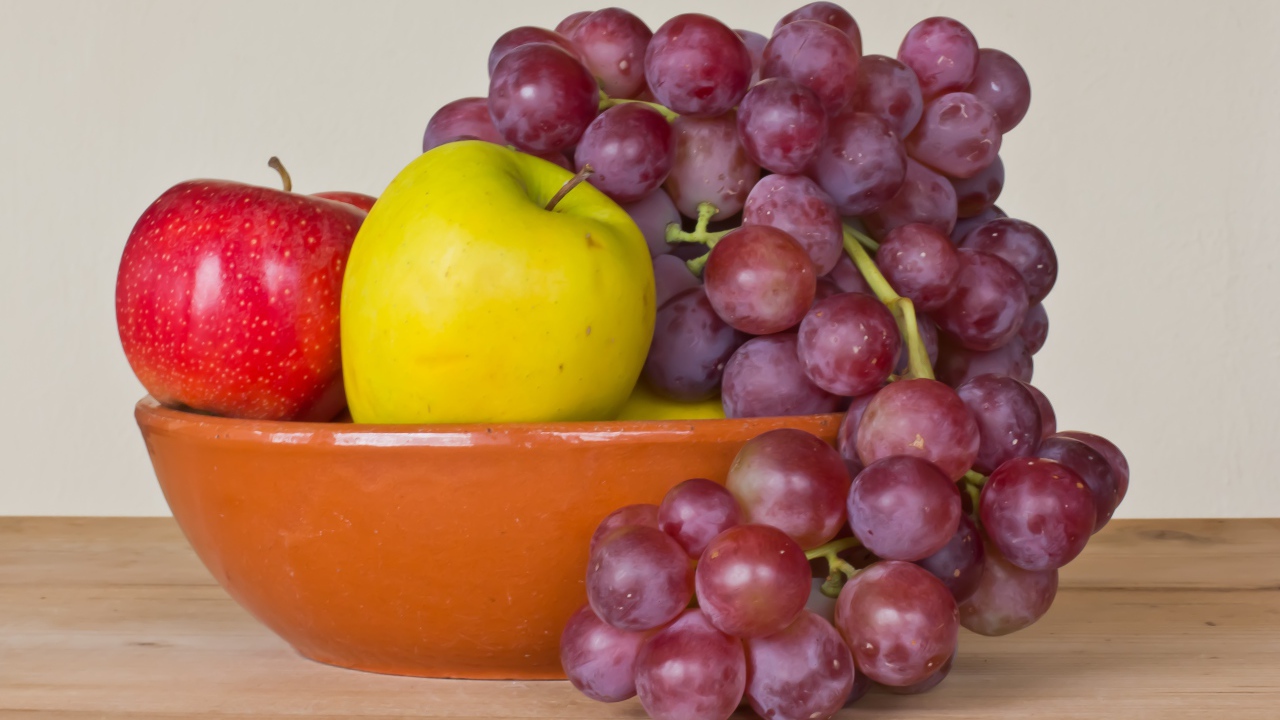 Яблоки и розовый виноград в тарелке на столе 