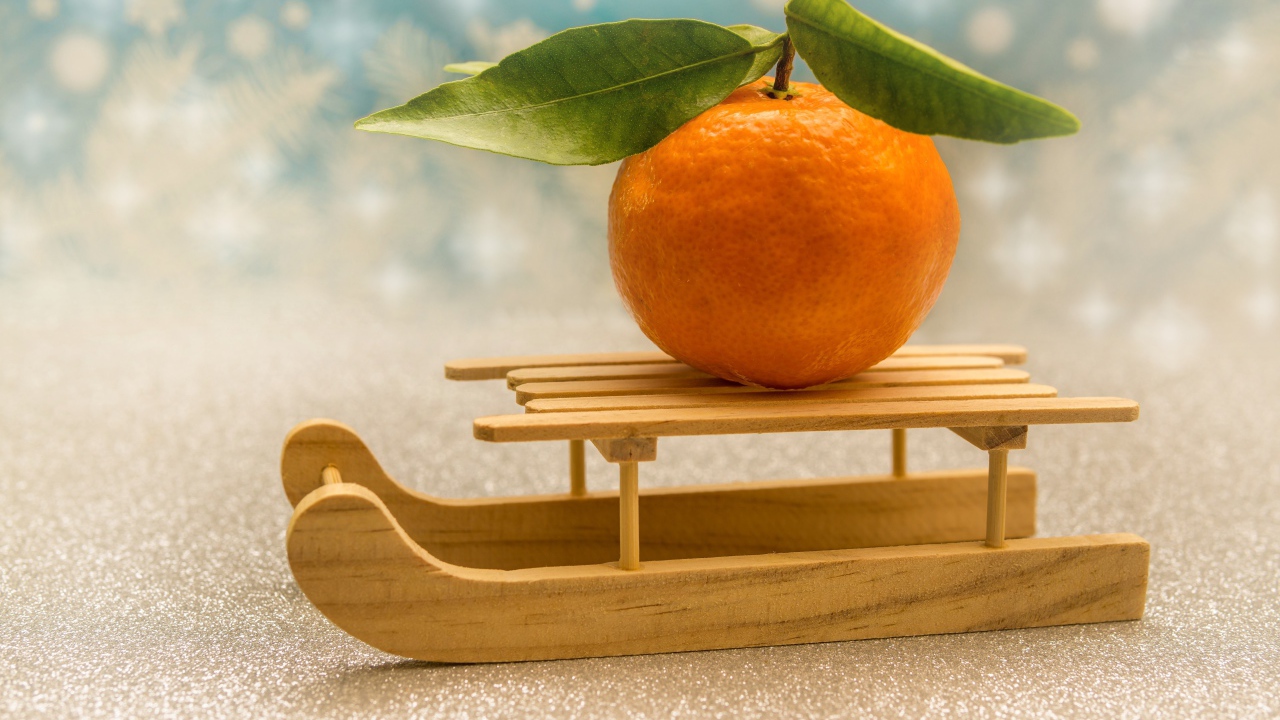 Большой оранжевый мандарин на маленьких санках