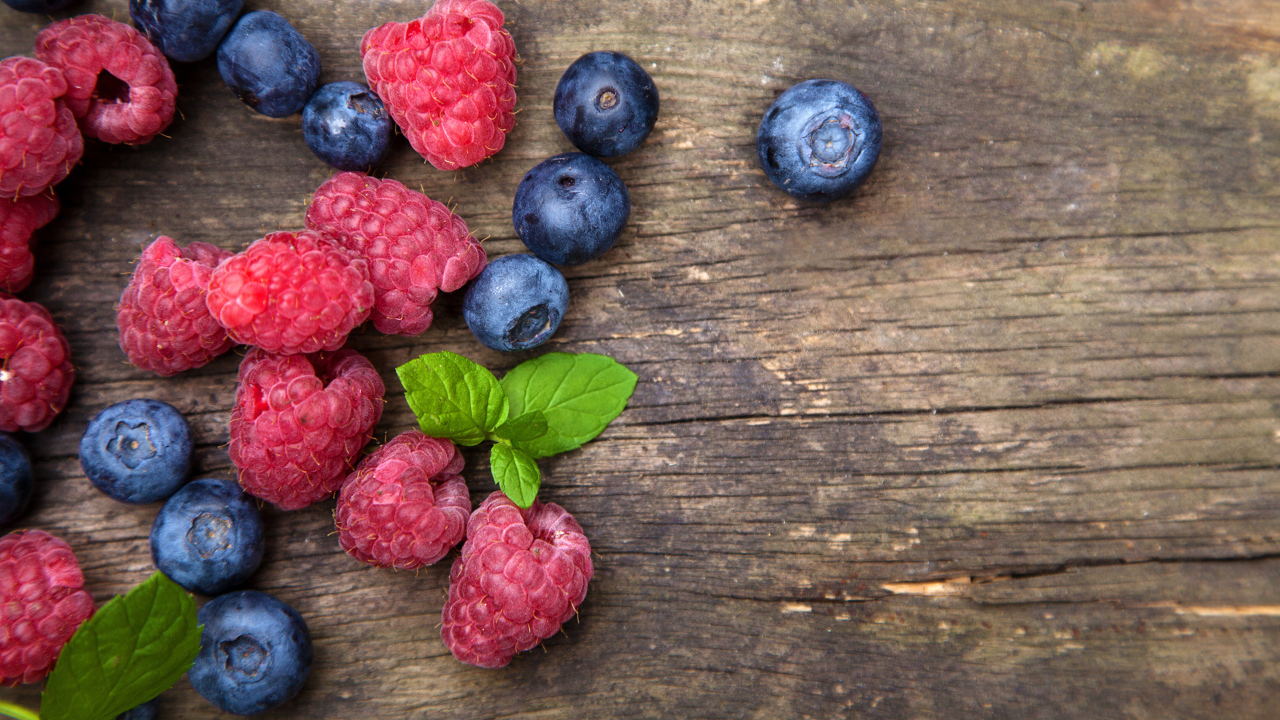 Голубые ягоды черники и красные ягоды малины на деревянном столе