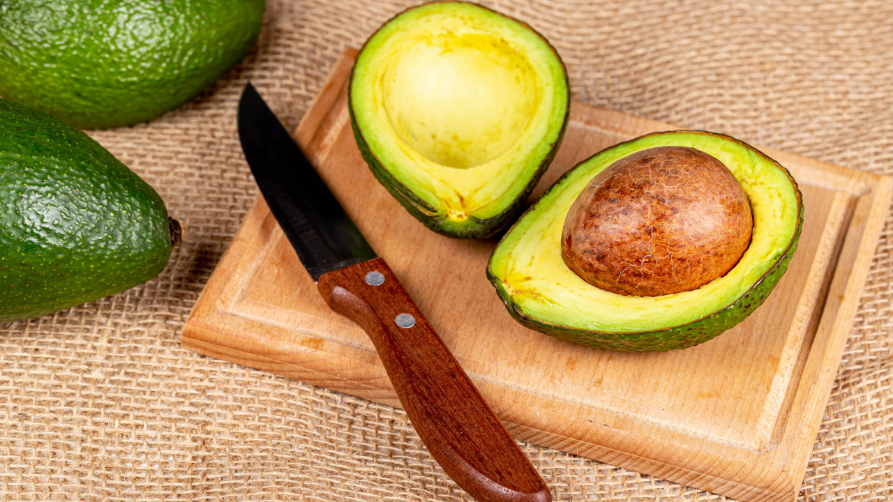 Зеленое авокадо с ножом на разделочной доске