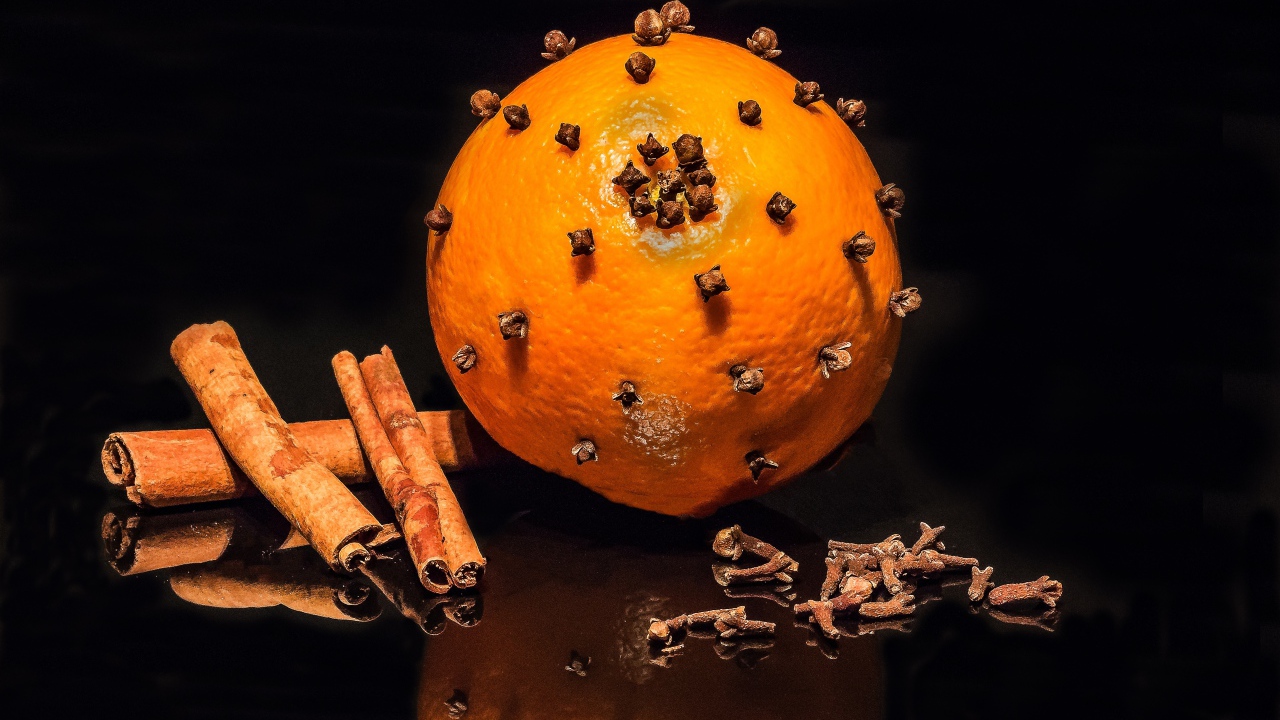 Оранжевый апельсин с гвоздикой и корицей на черном фоне 