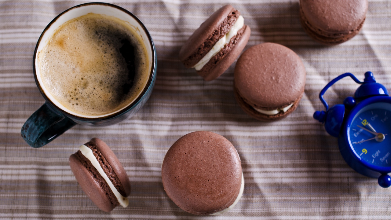 Чашка кофе на столе с десертом макарун и будильником