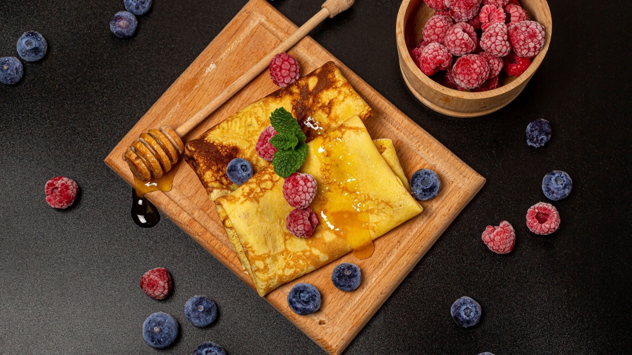 Блины с медом и ягодами черники и малины на черном столе 