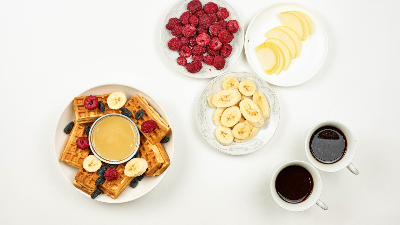 Сладкие вафли с малиной и бананами на столе  с кофе