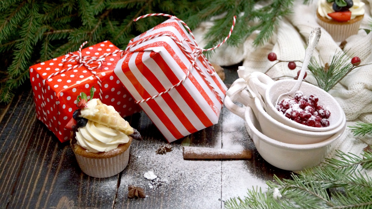 Два подарка на столе с еловой веткой и кексами 