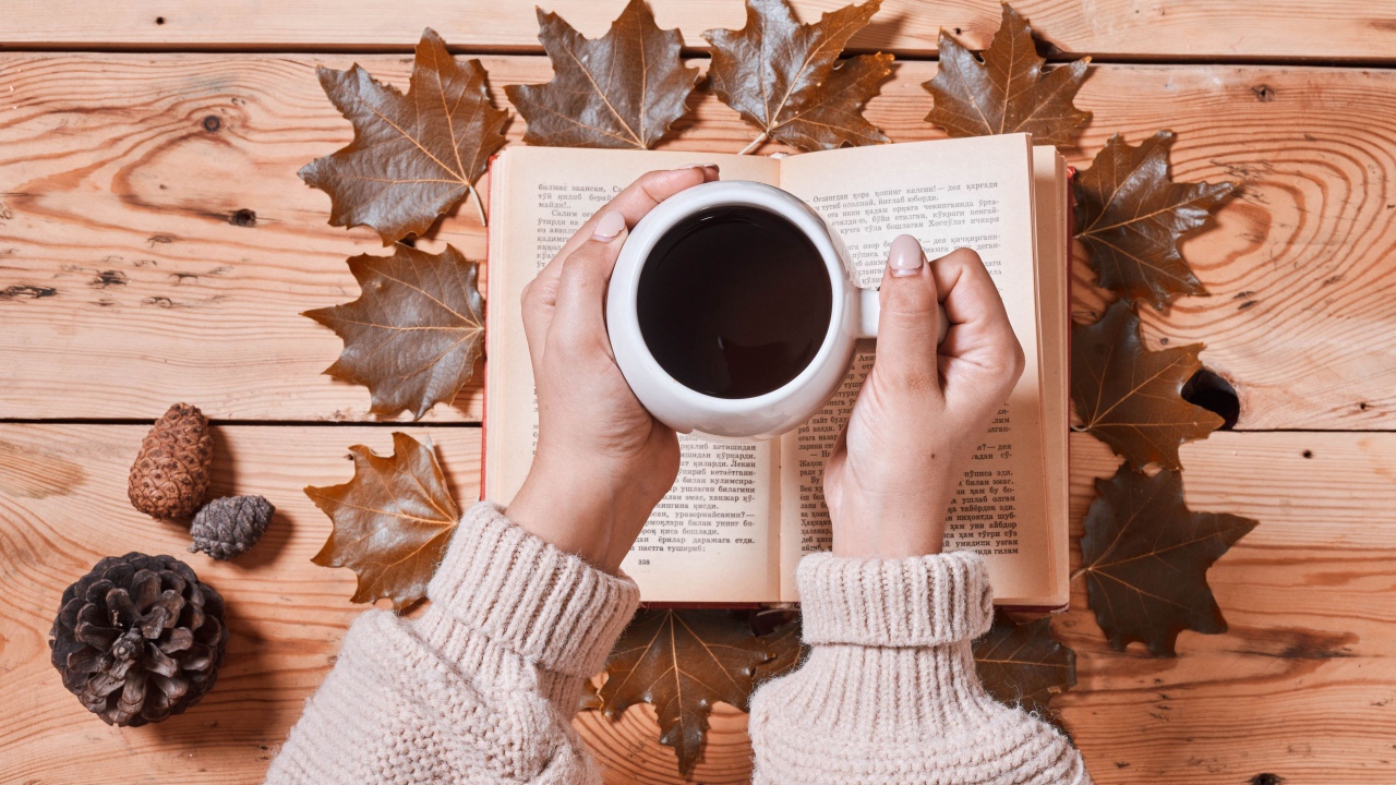 Чашка кофе в руках на столе с книгой и листьями