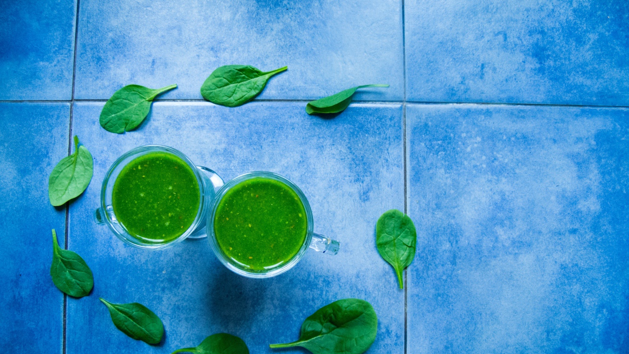 Два зеленых смузи с листьями базилика на голубом фоне