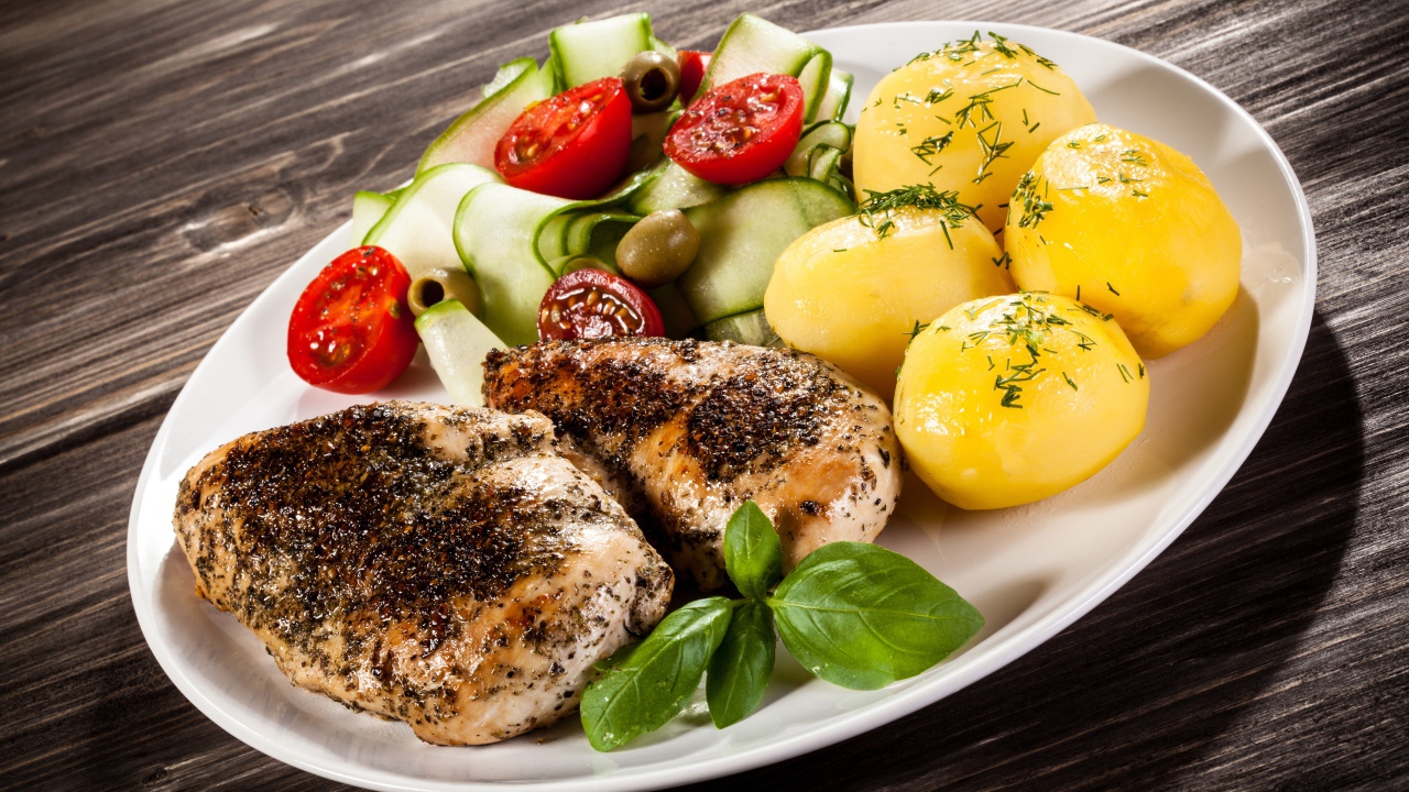 Куски курицы на тарелке с картофелем, помидорами и кабачком 