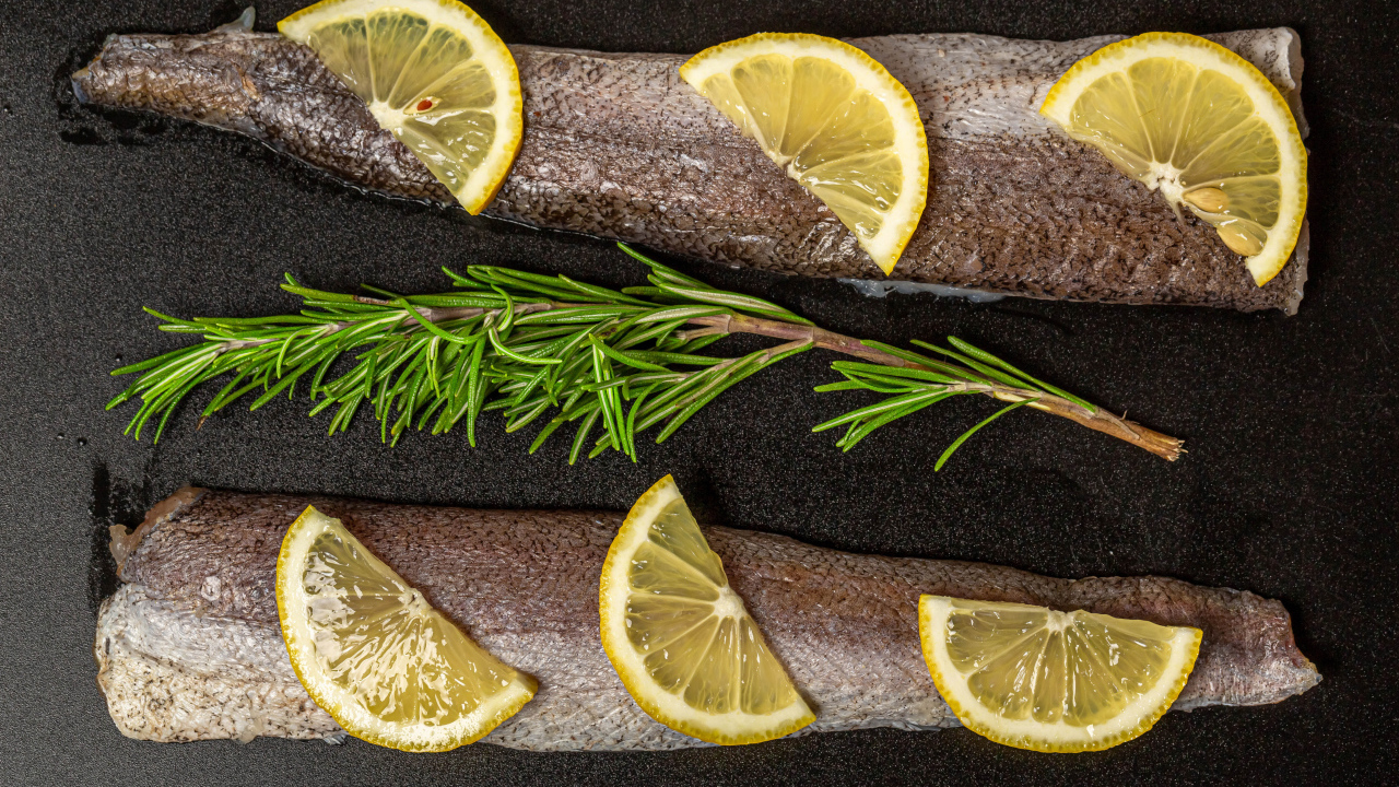 Свежее филе рыбы с лимоном и розмарином на черном фоне