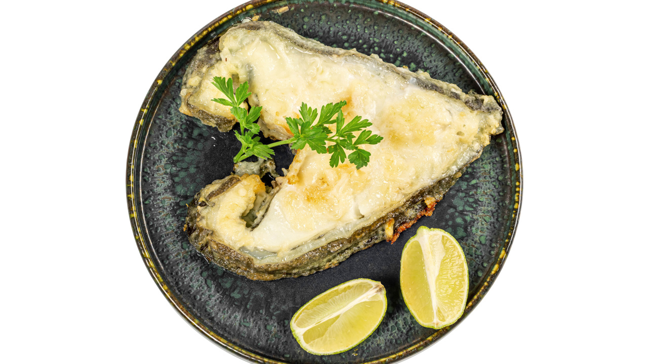 Кусок рыбы на тарелке с лимоном на белом фоне