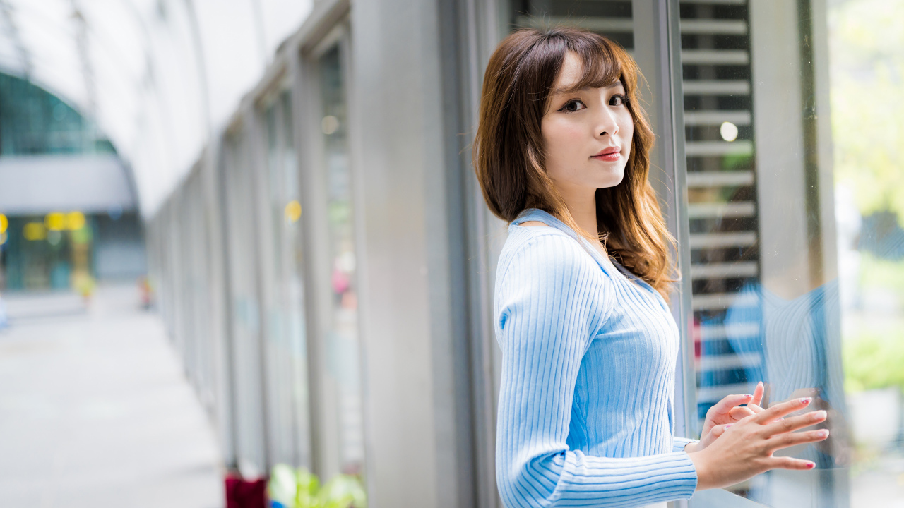 Красивая девушка азиатка в в голубой кофте стоит уокна