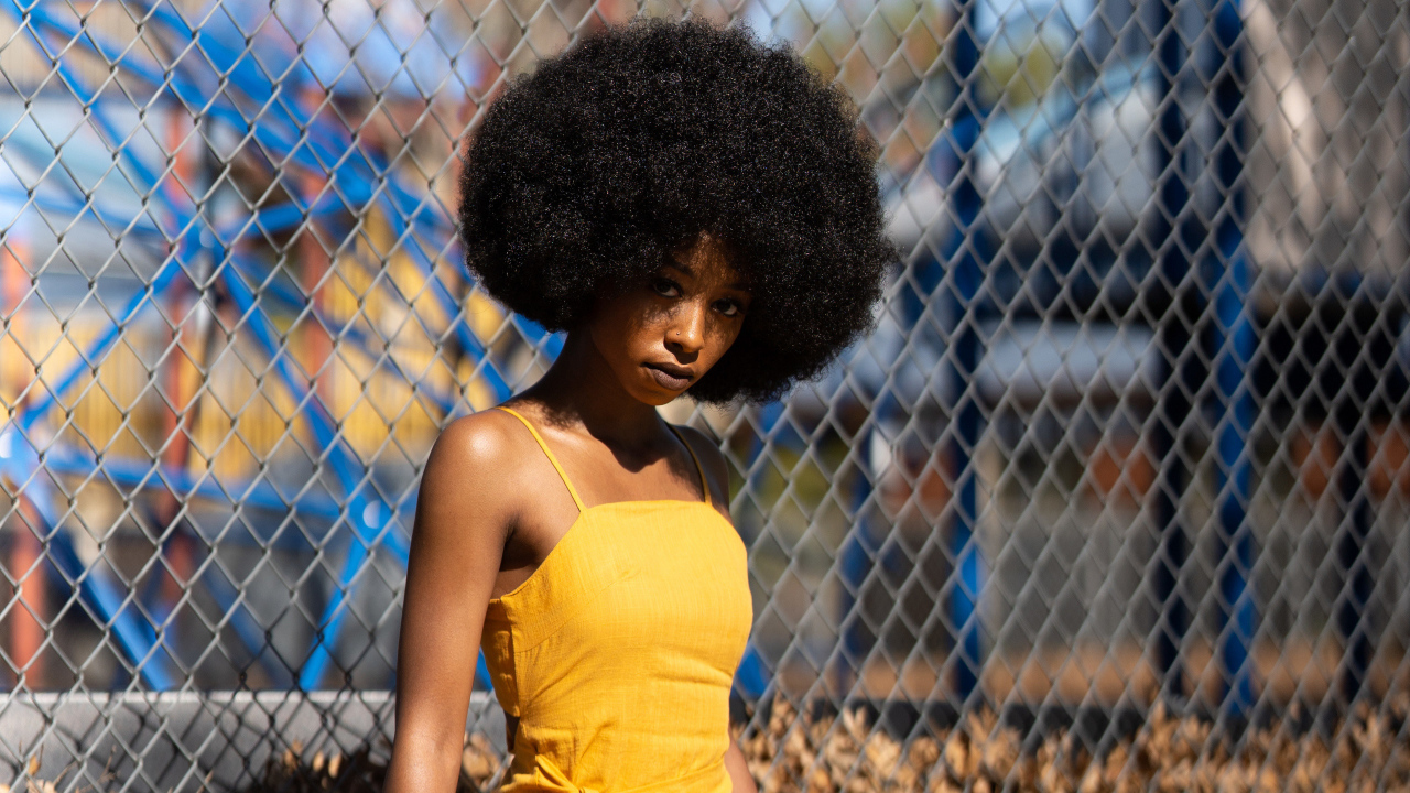 Темнокожая девушка в желтом платье стоит у сетки