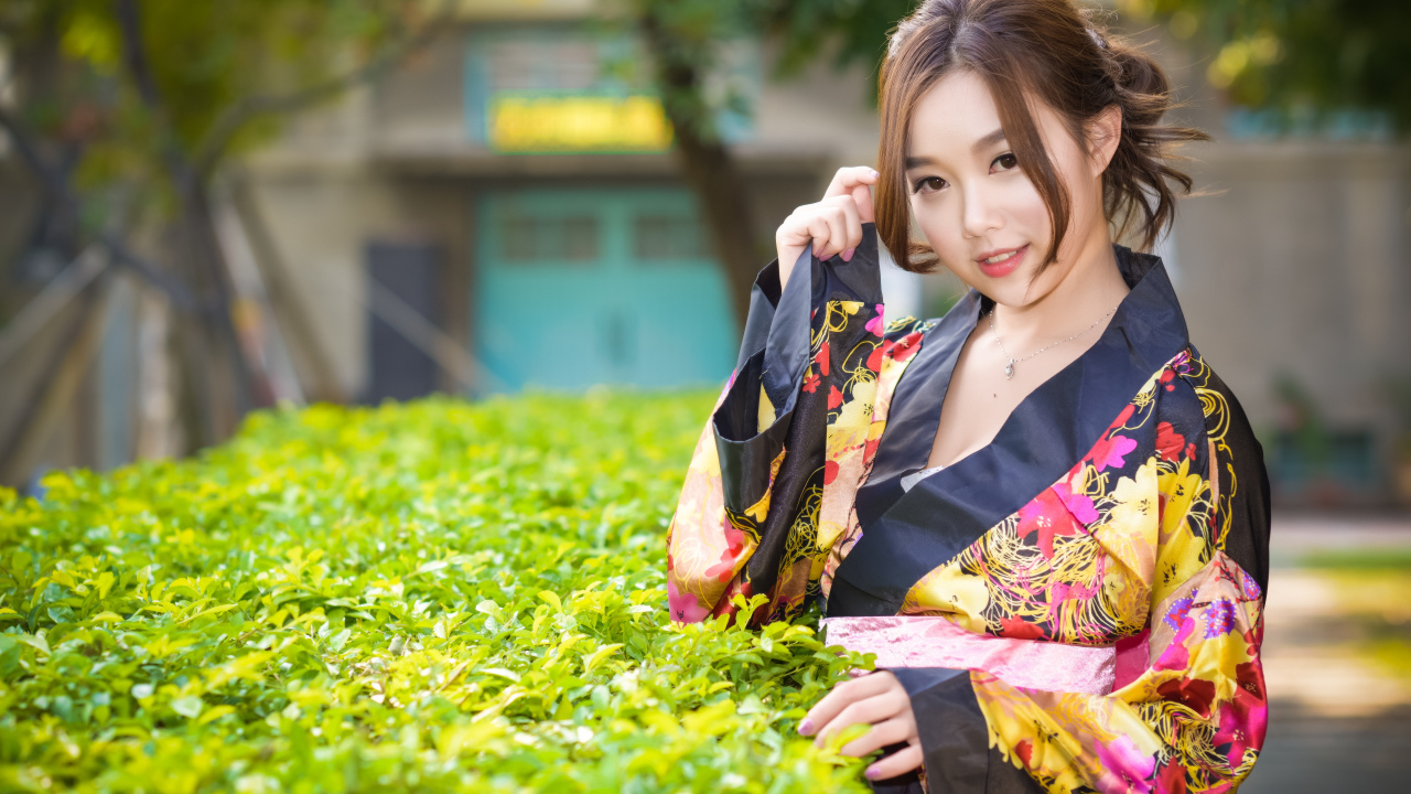 Девушка в кимоно стоит у зеленого куста