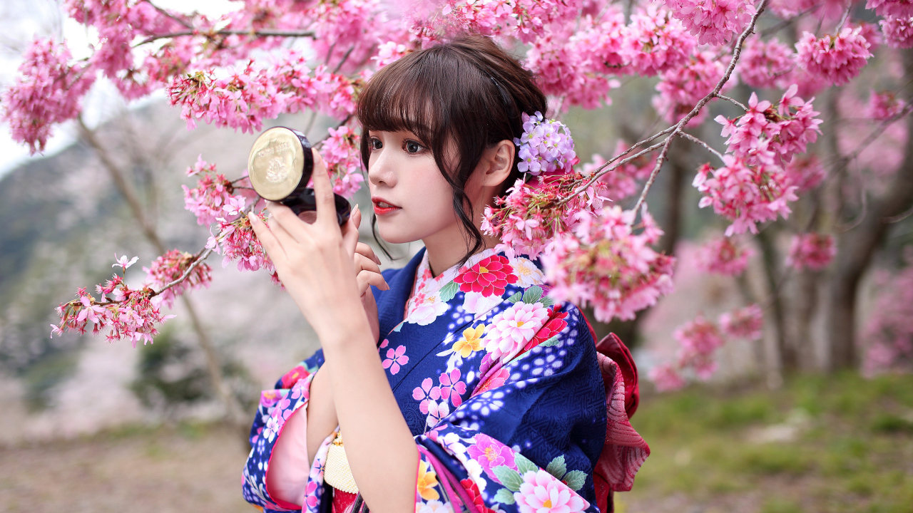Девушка в кимоно стоит у куста сакуры