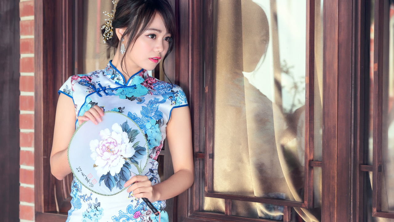 Девушка азиатка в красивом платье стоит у окна 