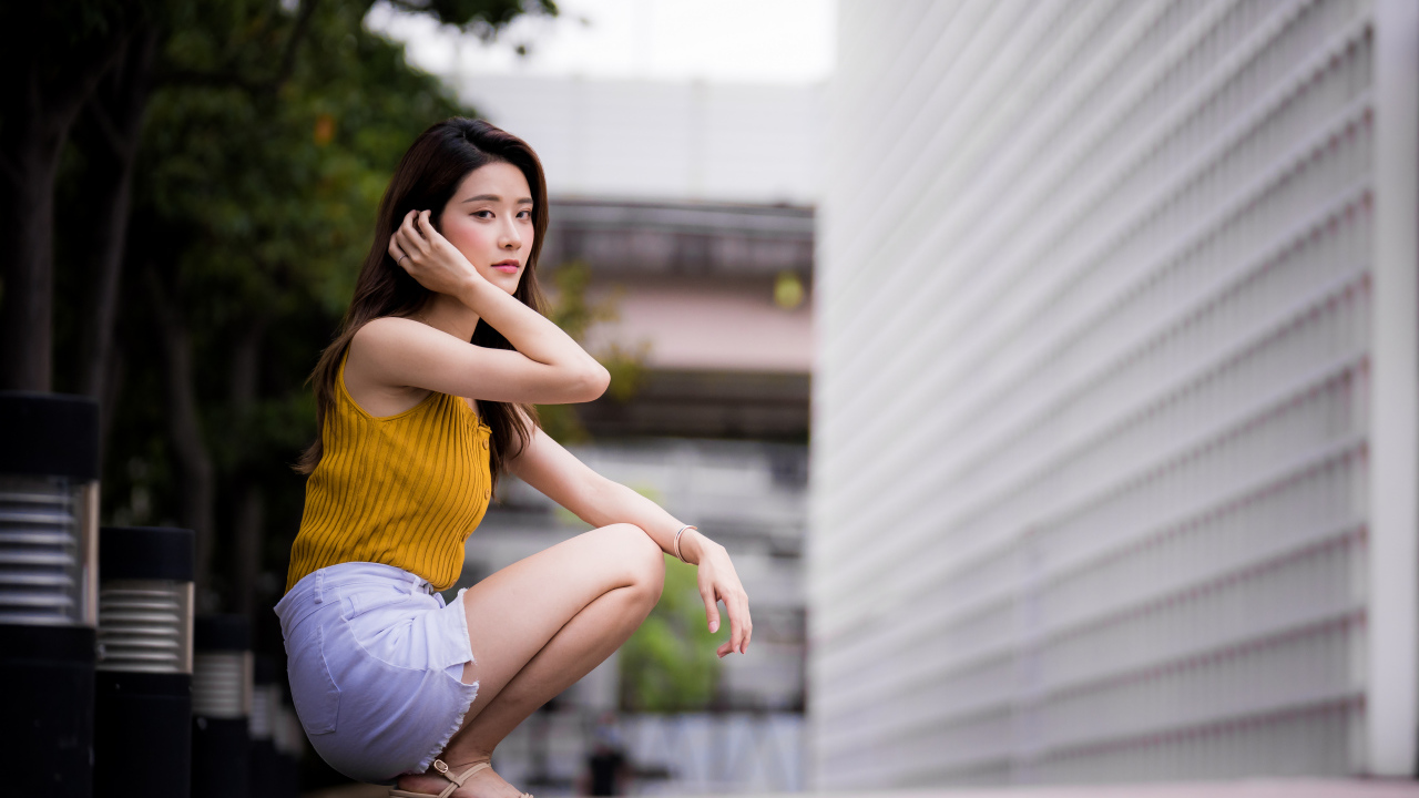 Девушка азиатка сидит на корточках у стены