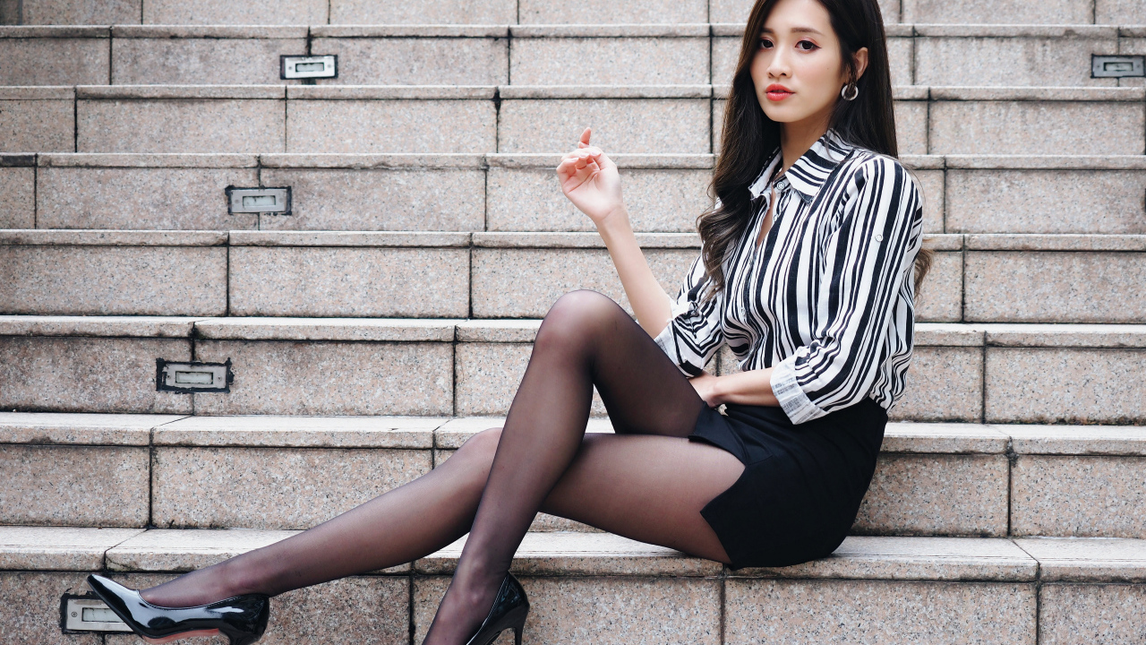 Красивая девушка азиатка в юбке сидит на ступеньках
