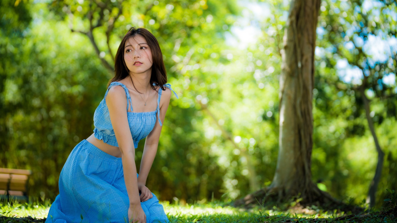 Красивая азиатка в голубом платье сидит на траве в парке 