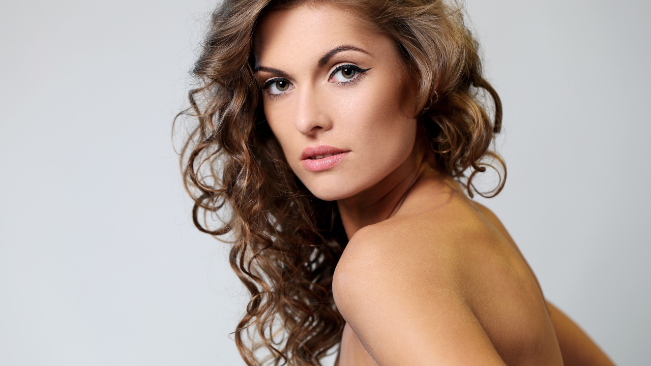 Вьющиеся волосы у красивой девушки на сером фоне
