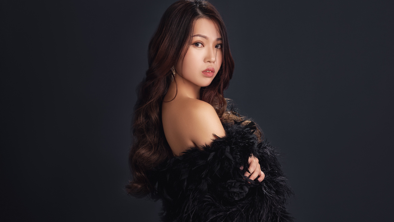 Милая девушка азиатка в черном наряде на сером фоне