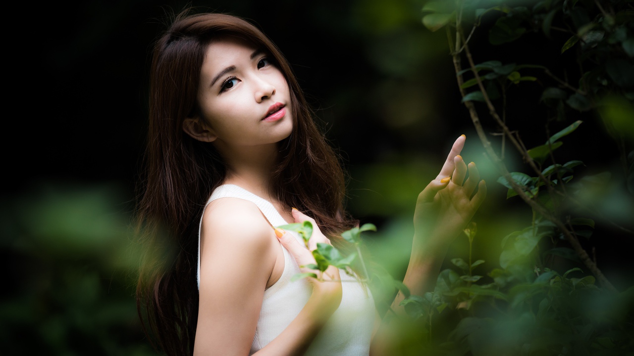 Милая азиатка в белом стоит у зеленых листьев