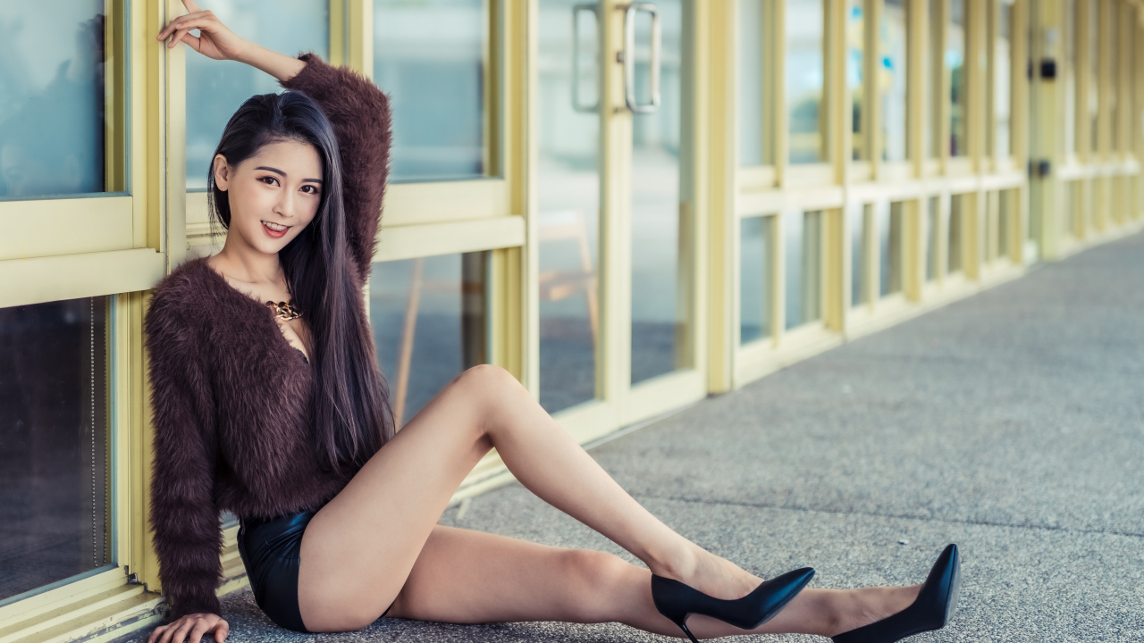 Девушка в свитере сидит у стеклянной стены 