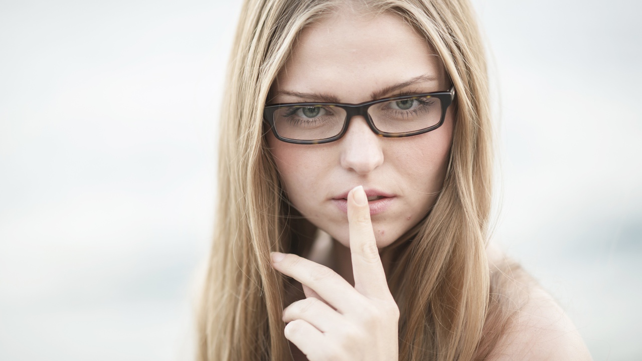 Девушка в очках с пальцем у лица