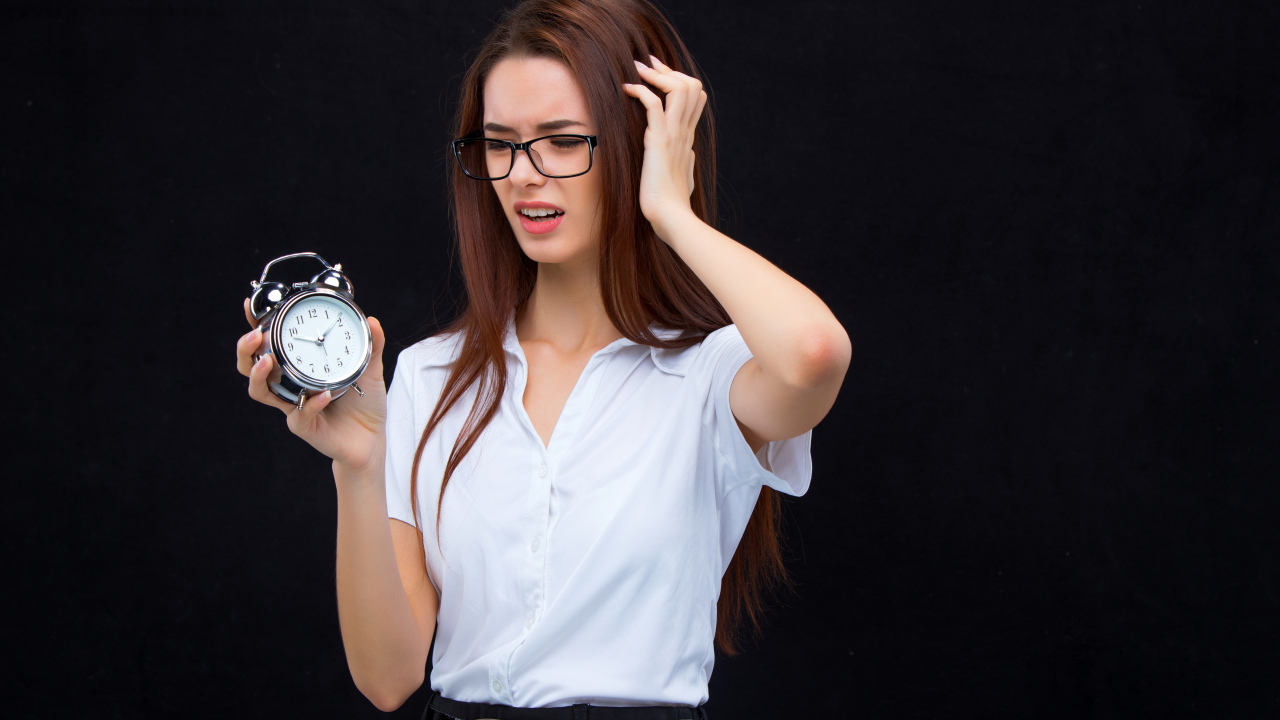 Девушка с головной болью с будильником в руке на черном фоне