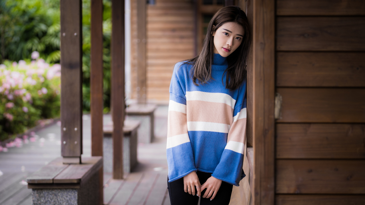 Грустная девушка азиатка в свитере у стены 