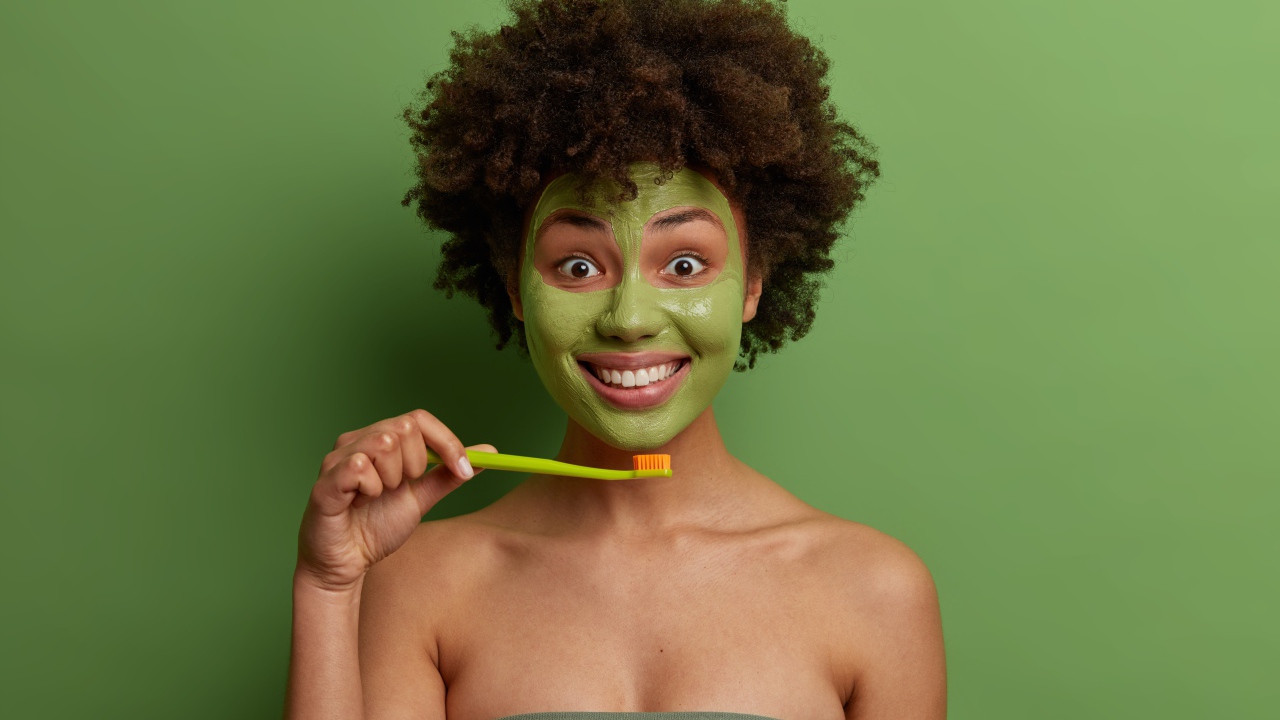 Улыбающаяся девушка с маской на лице чистит зубы