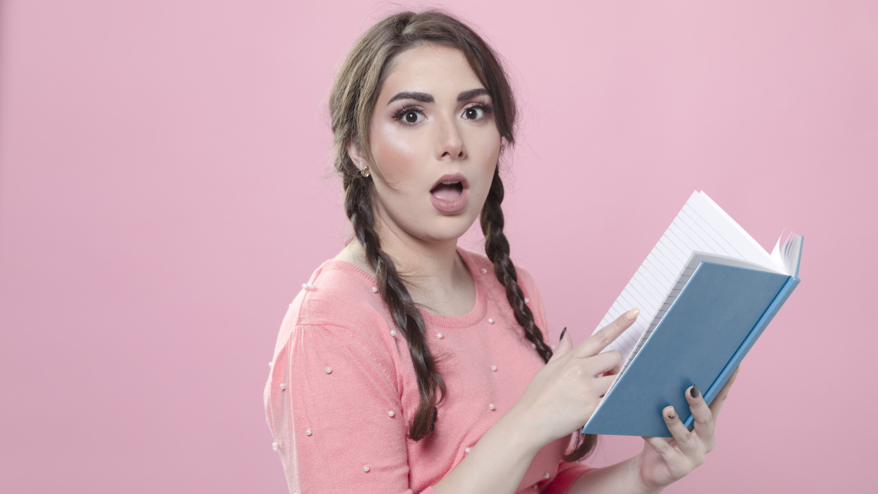 Удивленная девушка с книгой на розовом фоне