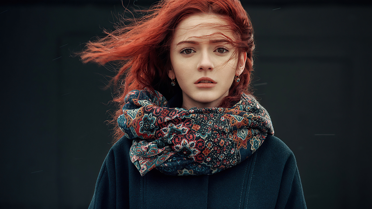 Ветер развивает волосы рыжеволосой девушки в пальто