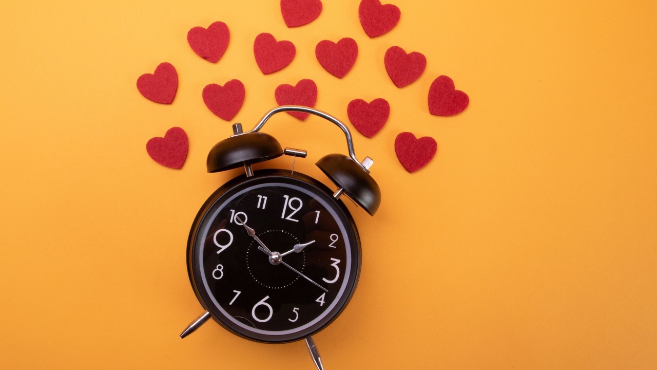 Черный будильник с сердечками на оранжевом фоне