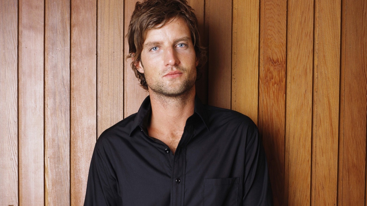 Красивый мужчина в черной рубашке на деревянном фоне