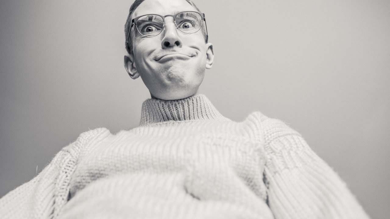 Мужчина в очках корчит лицо на сером фоне