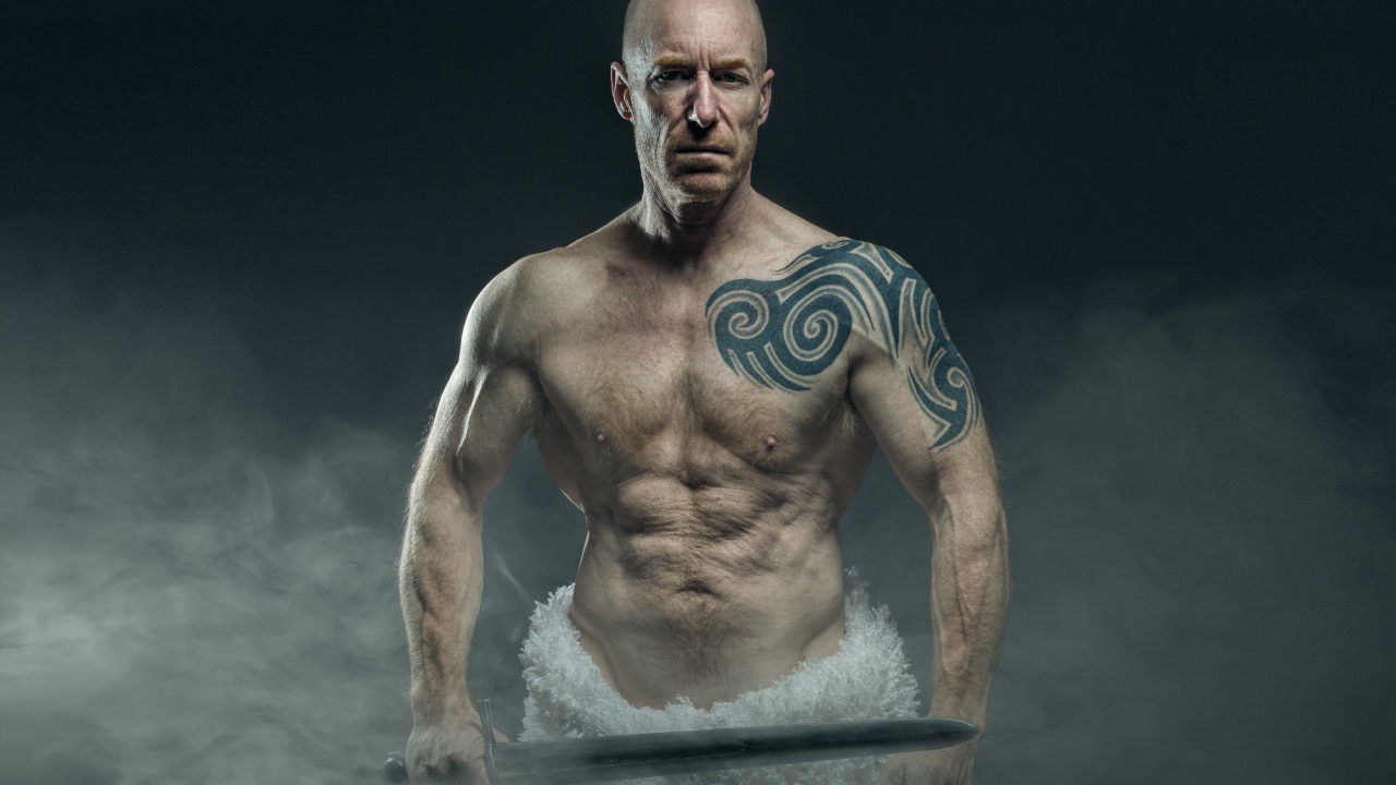Сильный мужчина с мечом с татуировками на теле 