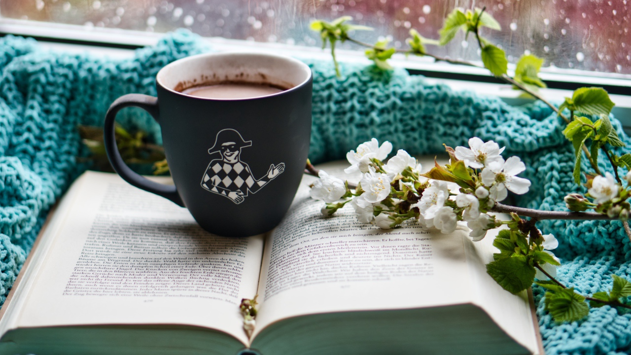 Цветущая ветка вишни на столе с книгой и чашкой кофе