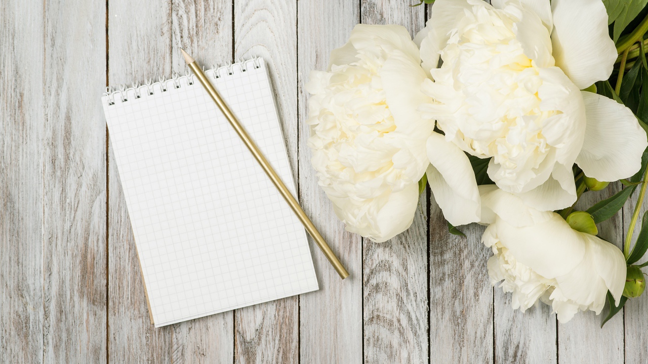Букет белых пионов с блокнотом и ручкой на деревянном фоне 