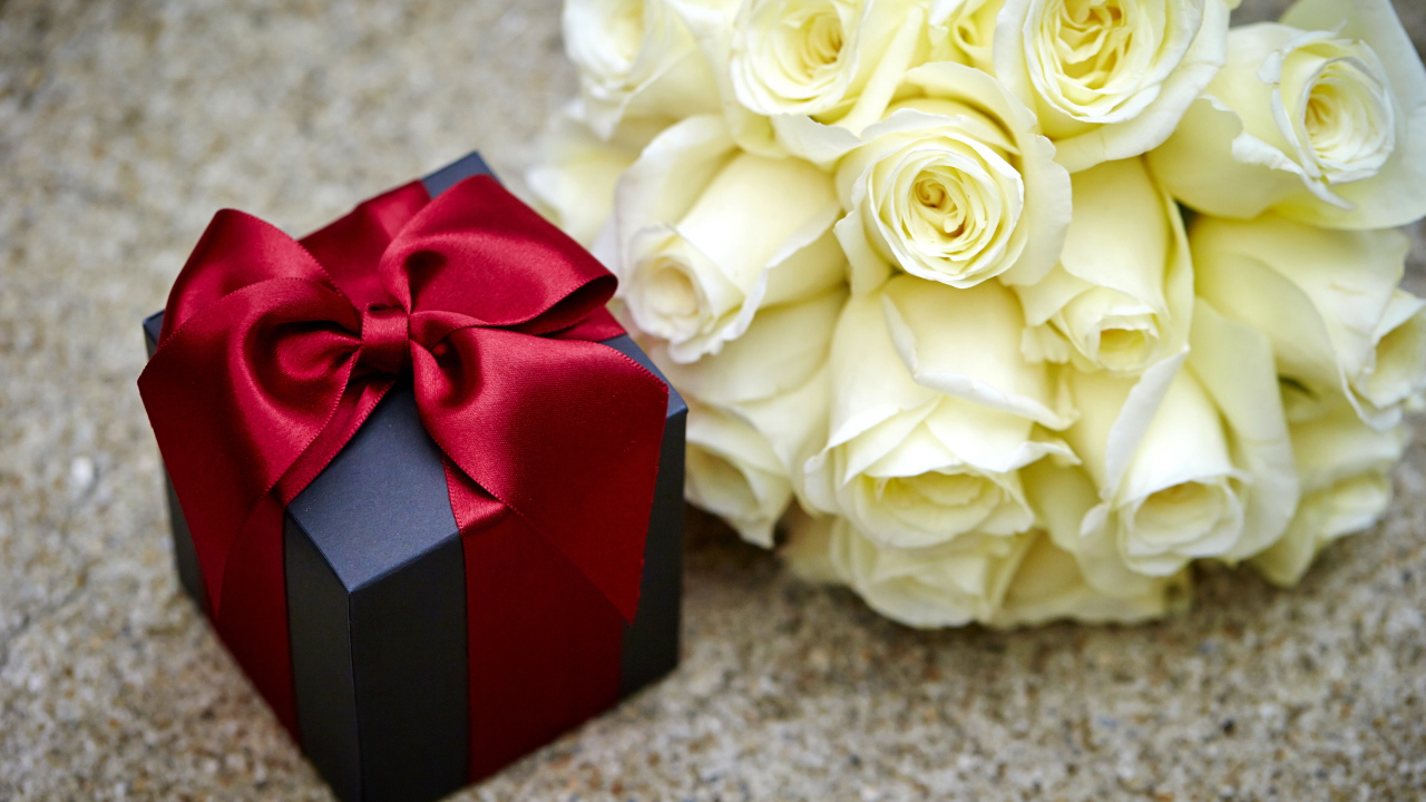 Букет белых роз с черным подарком на столе