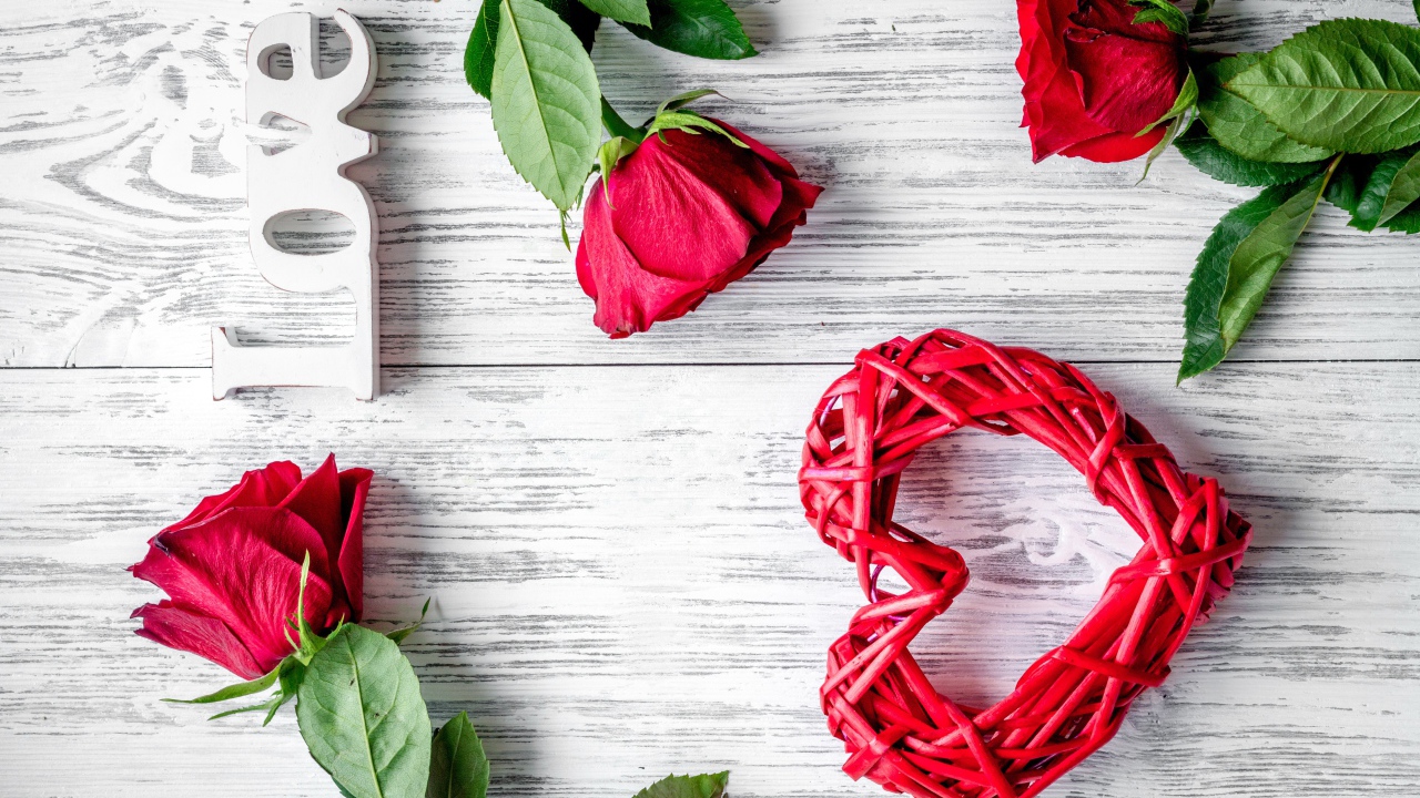 Красное плетеное сердце с алыми розами на деревянном столе