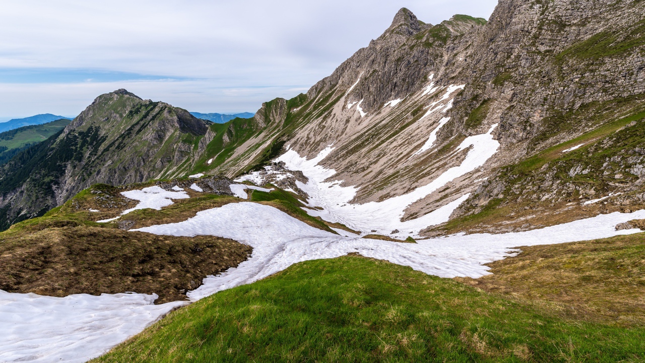 Снег на склонах горы с зеленой травой 