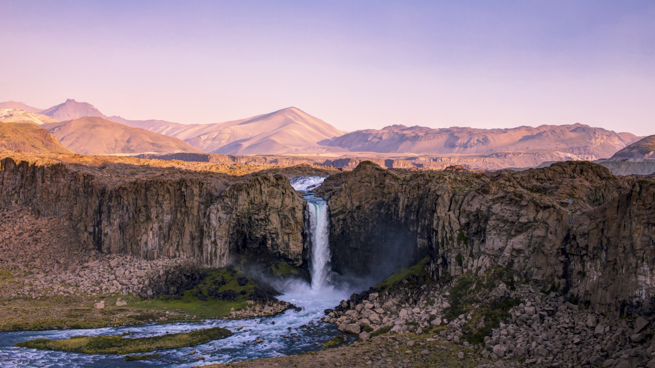 Водопад стекает по каменному склону горы на рассвете 