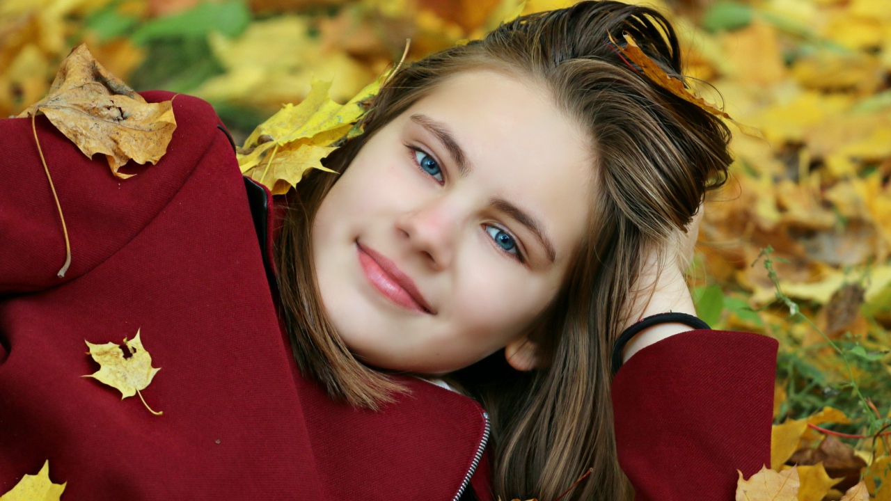 Красивая голубоглазая девочка лежит на опавшей листве