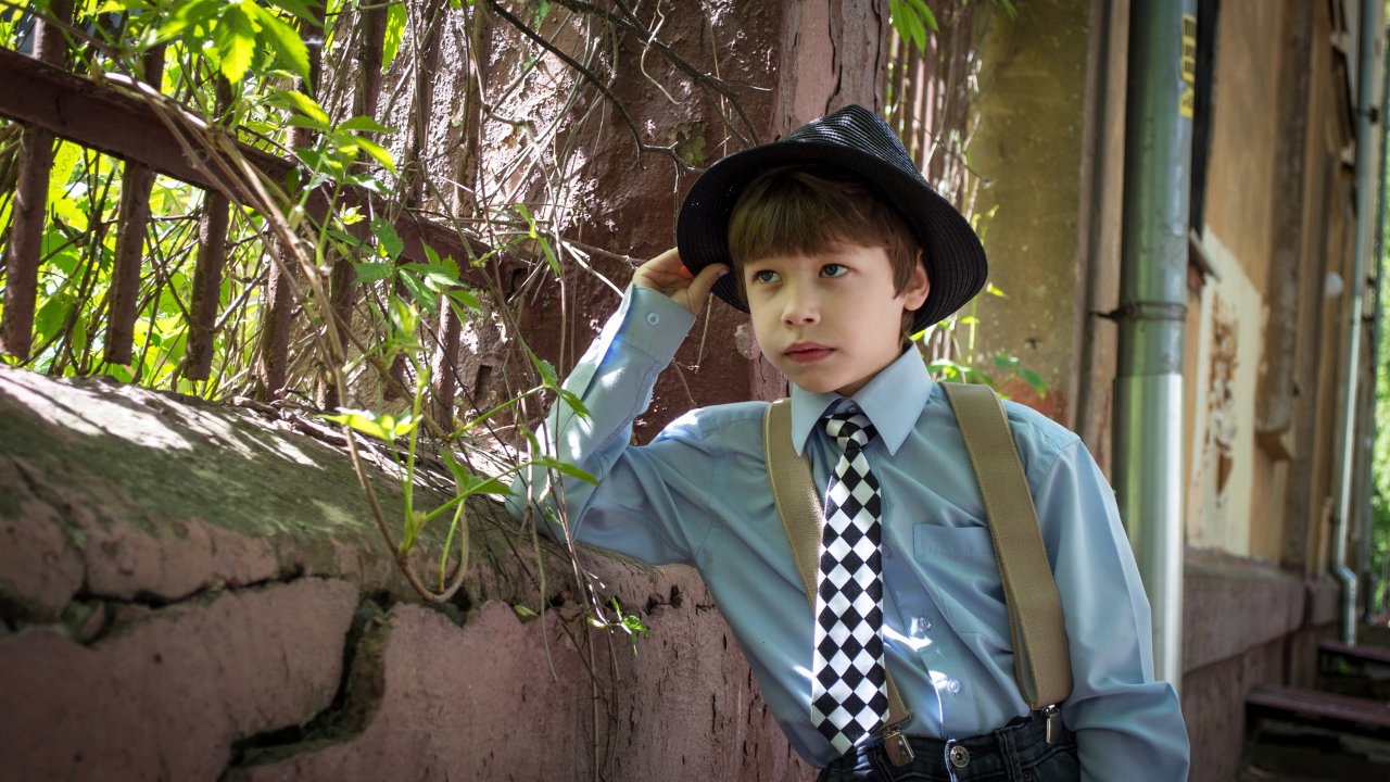 Красивый мальчик в шляпе стоит у забора 