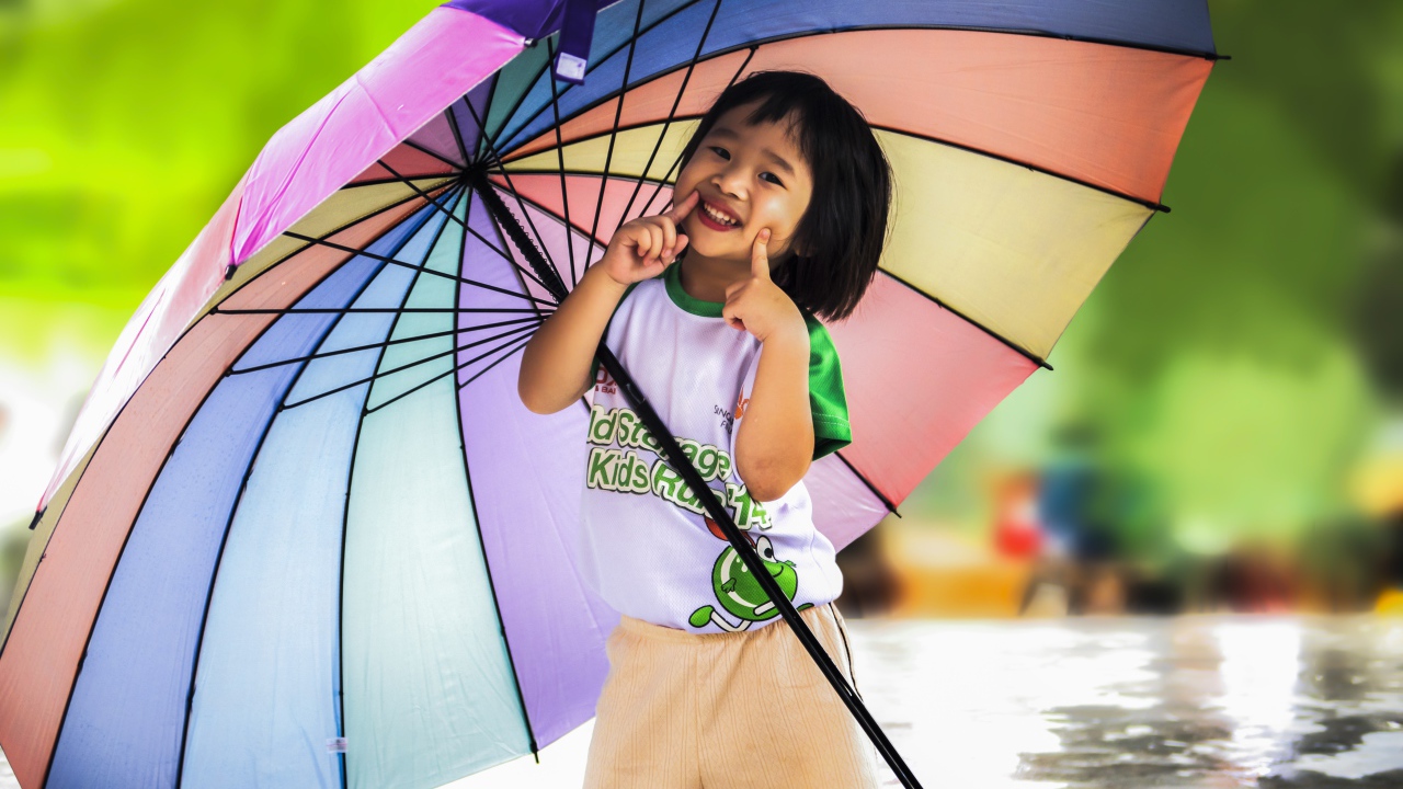 Маленькая девочка азиатка под большим разноцветным зонтом 