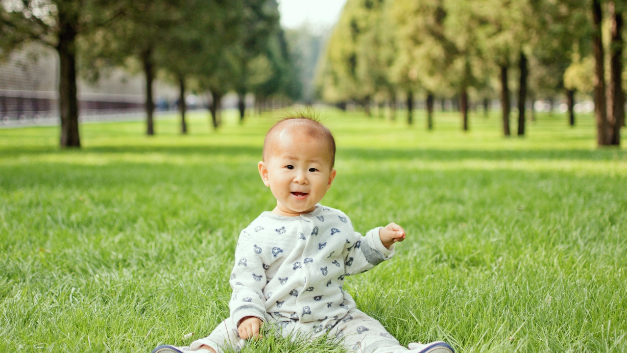 Маленький ребенок азиат сидит на зеленой траве 