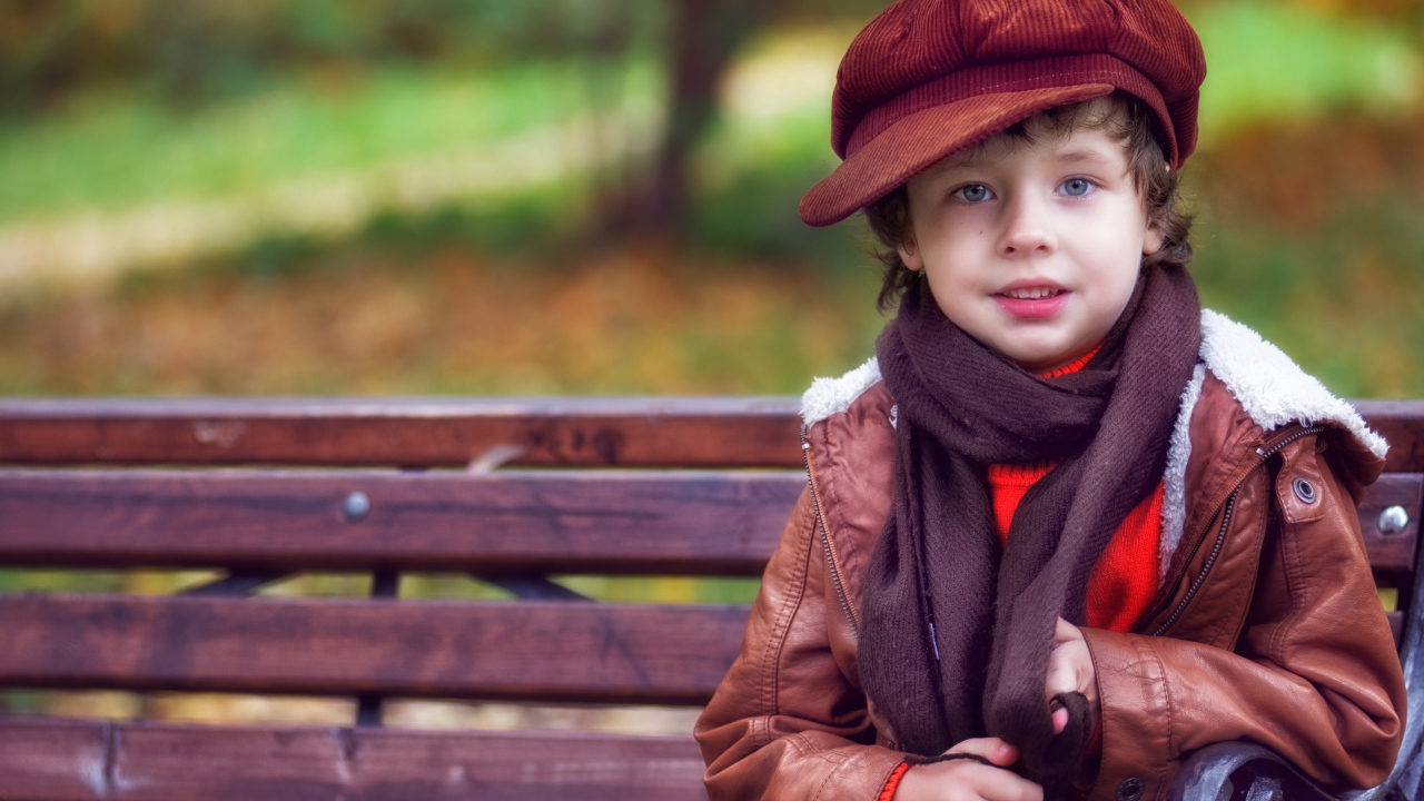 Маленький мальчик в кепке сидит на лавке