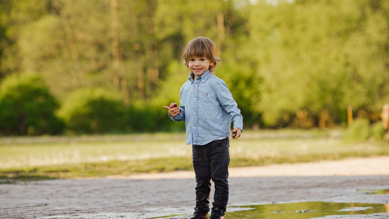 Маленький мальчик стоит в луже на дороге 