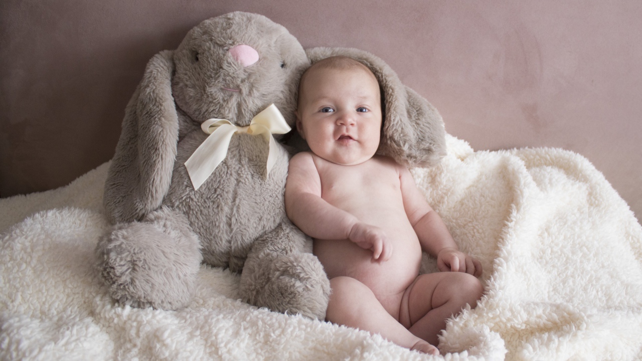 Маленький ребенок с игрушкой сидит у стены