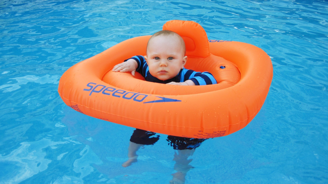 Маленький ребенок с оранжевым спасательным кругом в бассейне